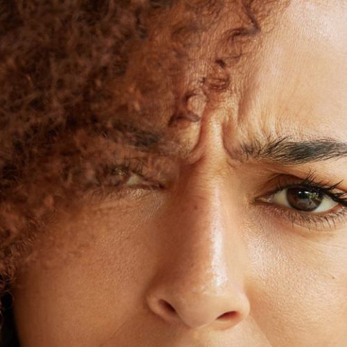 Close up portrait of puzzled discontent female with dark pure healthy skin and frizzy hair, looks in