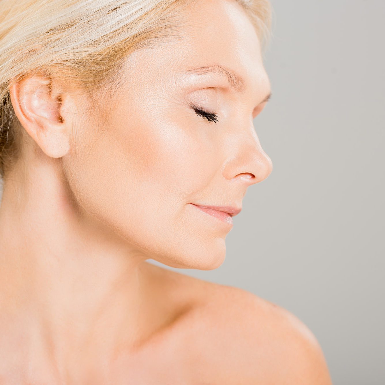 side view of attractive and blonde mature woman with closed eyes isolated on grey